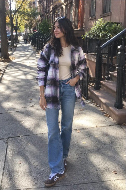 Woman wearing a plaid shacket over a cream fitted T-shirt with blue wide-leg jeans and brown casual sneakers on a New York sidewalk