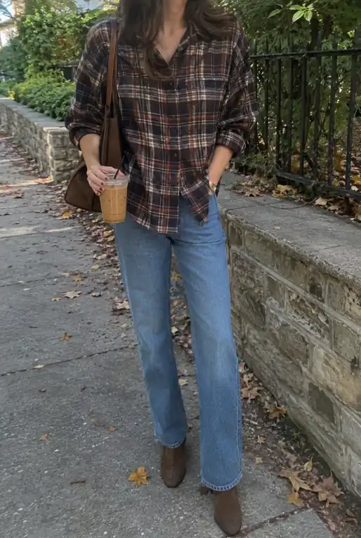 Woman wearing a dark brown plaid shirt with light-wash straight-leg jeans, brown ankle boots, and a brown shoulder bag for fall.