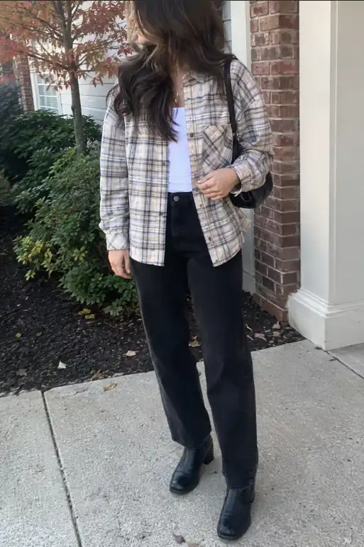 Woman wearing a neutral plaid shirt over a white top with black straight-leg pants, black ankle boots, and a black backpack.