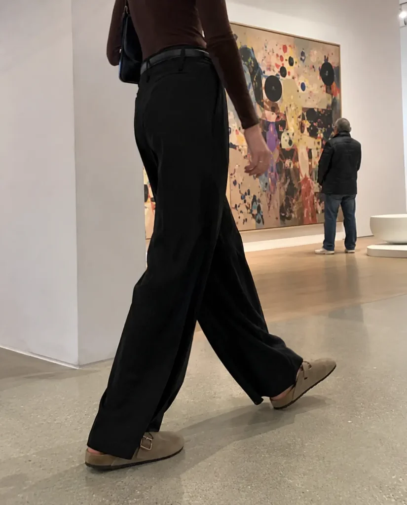 Woman wearing beige wide-leg trousers with taupe leather clogs at an outdoor cafe