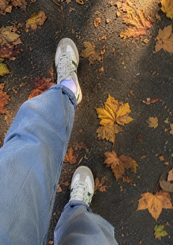 Woman wearing light wash wide leg jeans with white and green retro sneakers on an autumn park path